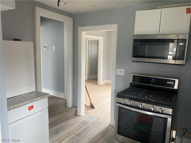 kitchen with appliances with stainless steel finishes, wood-type flooring, and white cabinetry