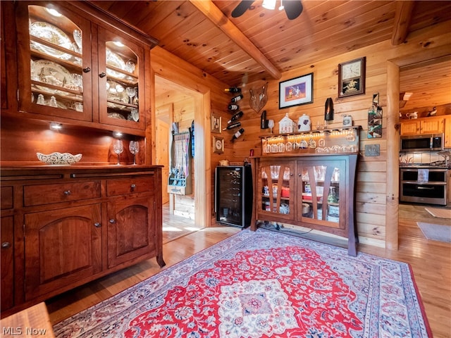 interior space with wood walls, beam ceiling, ceiling fan, and light wood-type flooring