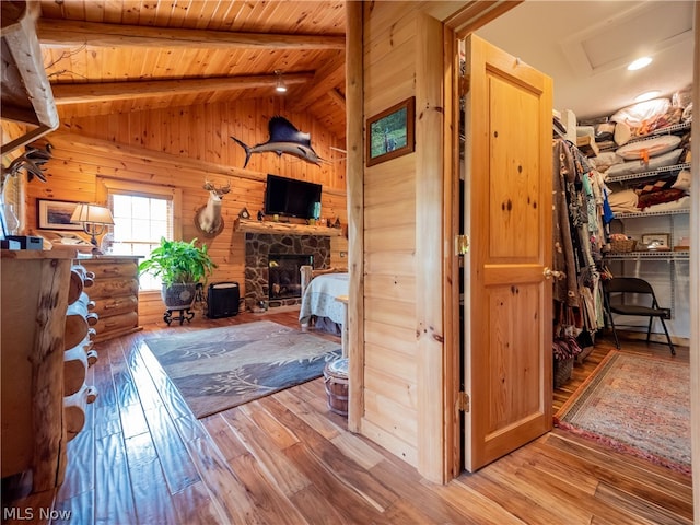 bedroom with wooden walls, light hardwood / wood-style flooring, vaulted ceiling with beams, wood ceiling, and a stone fireplace