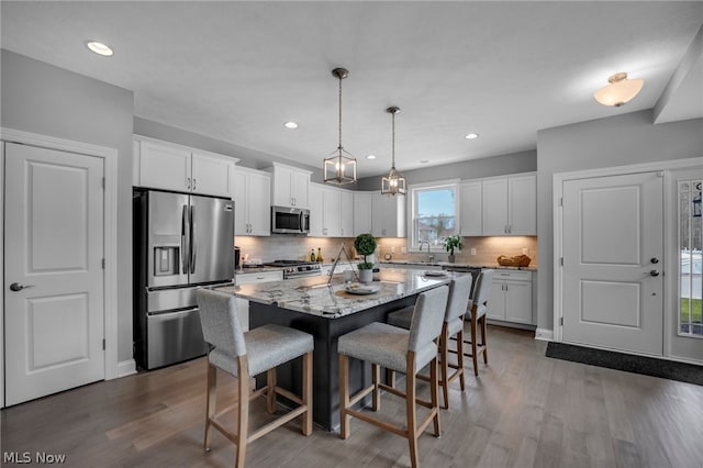 kitchen with appliances with stainless steel finishes, backsplash, hanging light fixtures, dark hardwood / wood-style floors, and a center island