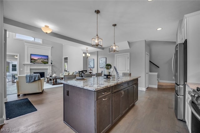 kitchen with dark brown cabinets, hardwood / wood-style floors, pendant lighting, and a center island with sink