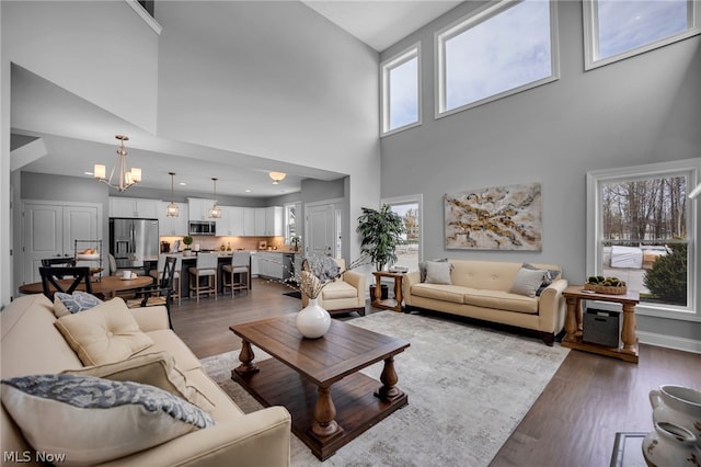 living room with a chandelier, dark wood-type flooring, and a towering ceiling