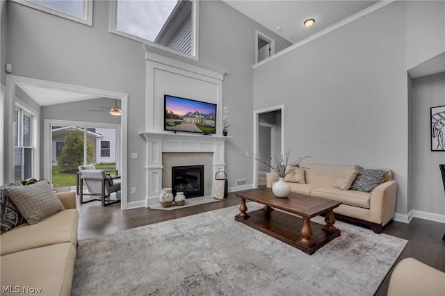 living room with dark hardwood / wood-style floors, ceiling fan, a high end fireplace, and a high ceiling