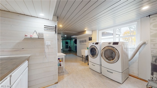 clothes washing area with wood ceiling, cabinets, washing machine and clothes dryer, light hardwood / wood-style flooring, and wooden walls