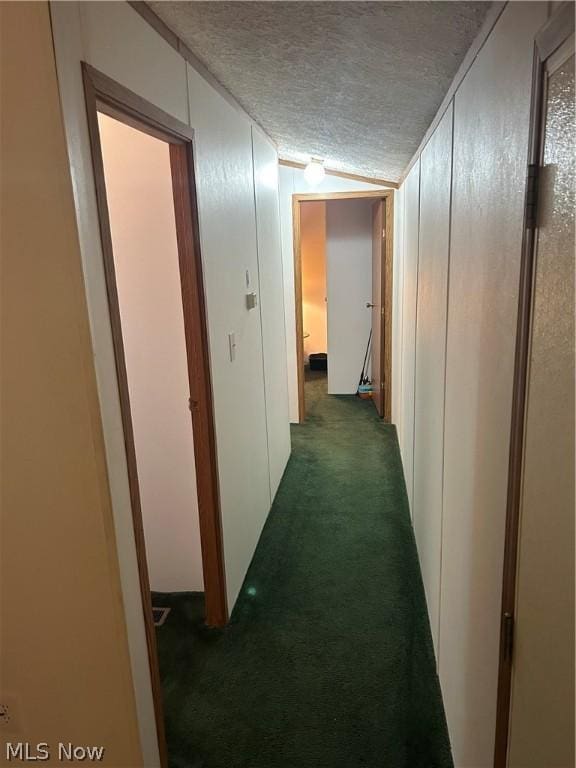 hallway featuring dark colored carpet, lofted ceiling, and a textured ceiling