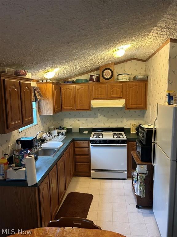 kitchen with sink, white appliances, vaulted ceiling, and a textured ceiling