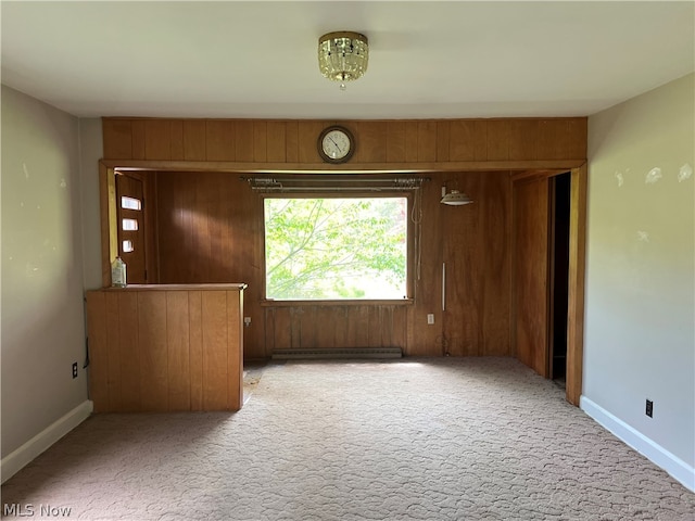 carpeted spare room featuring wooden walls and a baseboard heating unit