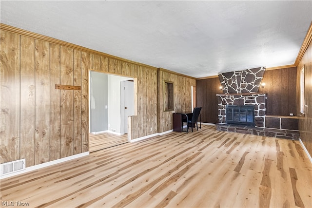 unfurnished room featuring wooden walls, ornamental molding, light hardwood / wood-style floors, and a fireplace