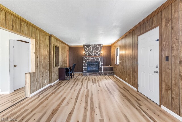 empty room featuring light hardwood / wood-style flooring, wood walls, and a stone fireplace