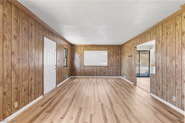 spare room with wooden walls, crown molding, a textured ceiling, and light wood-type flooring