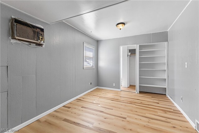 unfurnished bedroom featuring light wood-type flooring and an AC wall unit