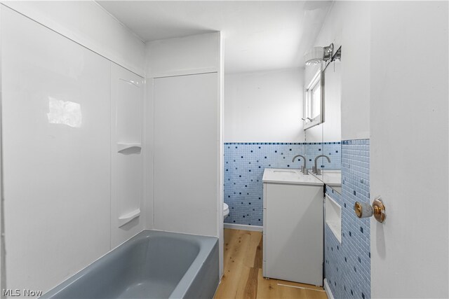 full bathroom with tile walls, toilet, vanity, hardwood / wood-style flooring, and bathing tub / shower combination