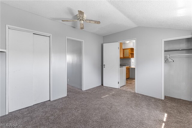 unfurnished bedroom featuring carpet floors, two closets, ceiling fan, a textured ceiling, and lofted ceiling