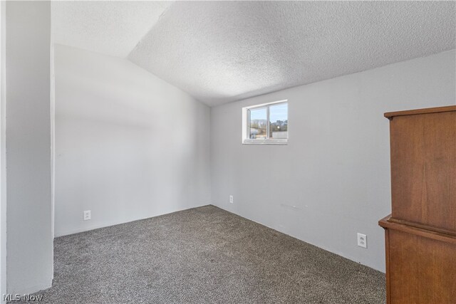 carpeted spare room featuring a textured ceiling and vaulted ceiling