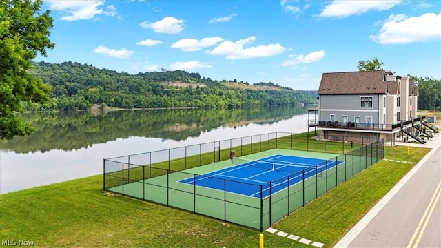 view of tennis court with a yard and a water view