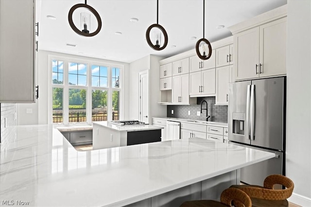 kitchen featuring appliances with stainless steel finishes, backsplash, sink, decorative light fixtures, and a kitchen island