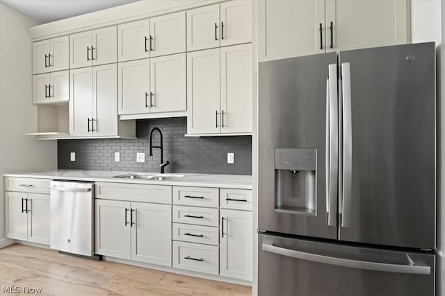 kitchen featuring white cabinets, sink, light hardwood / wood-style flooring, appliances with stainless steel finishes, and tasteful backsplash