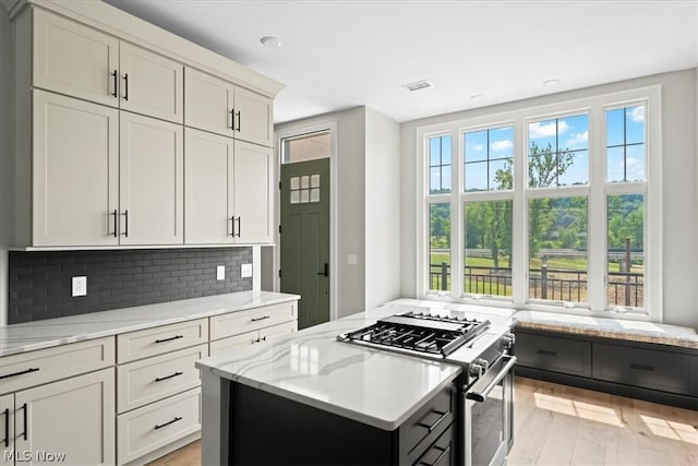 kitchen featuring light stone countertops, backsplash, high end stove, light hardwood / wood-style flooring, and a center island