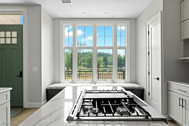 kitchen featuring white cabinets, light stone countertops, light hardwood / wood-style floors, and stainless steel gas cooktop