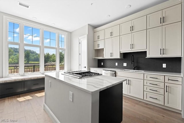 kitchen with light stone countertops, sink, stainless steel appliances, decorative backsplash, and a kitchen island