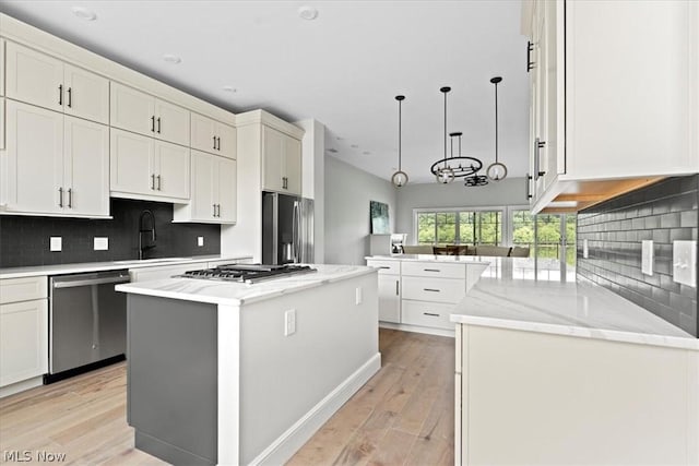 kitchen featuring kitchen peninsula, appliances with stainless steel finishes, light wood-type flooring, pendant lighting, and a center island