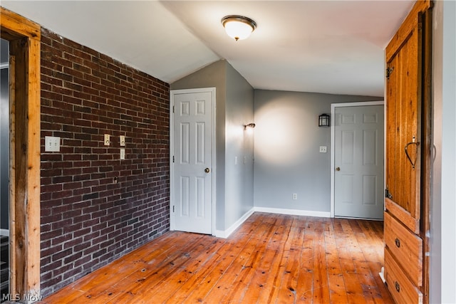 unfurnished room with brick wall, hardwood / wood-style flooring, and lofted ceiling