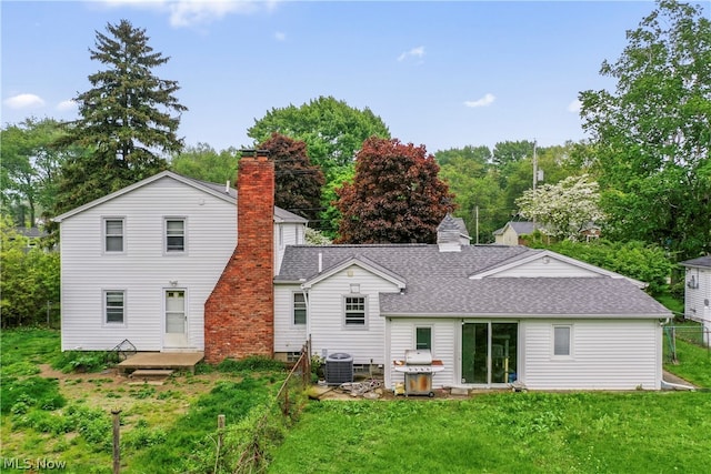 rear view of property with central air condition unit and a lawn