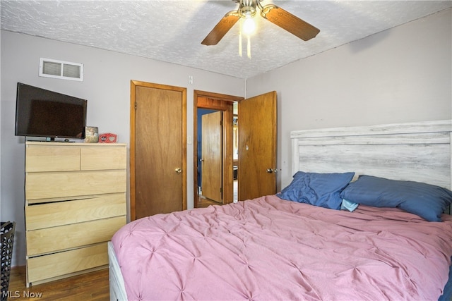 bedroom featuring dark hardwood / wood-style floors, ceiling fan, and a textured ceiling