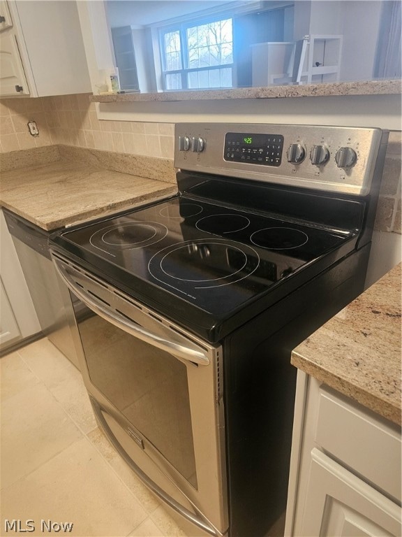 kitchen featuring light tile floors, electric stove, white cabinets, backsplash, and light stone countertops