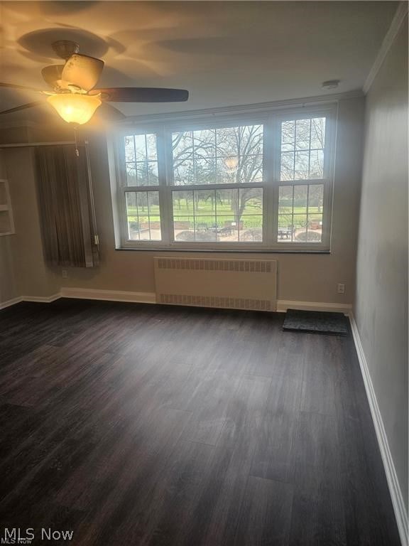 unfurnished room featuring a wealth of natural light, radiator, ceiling fan, and dark hardwood / wood-style flooring