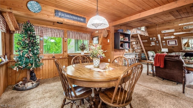 carpeted dining room featuring wooden walls, beamed ceiling, and wooden ceiling