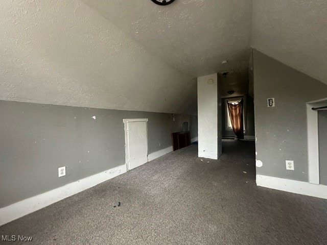 additional living space with dark colored carpet, a textured ceiling, and lofted ceiling