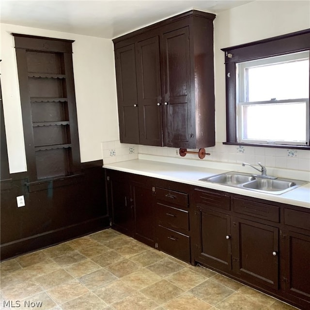 kitchen with tasteful backsplash, dark brown cabinets, sink, and light tile flooring