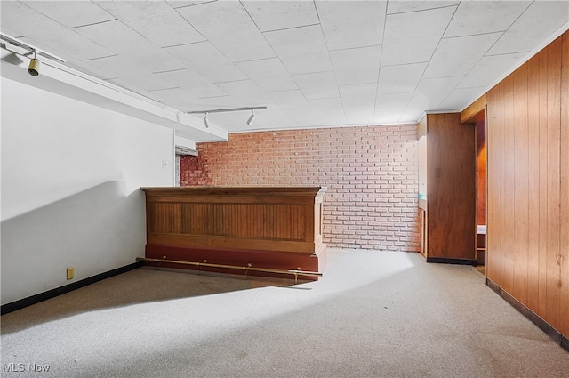 carpeted empty room with wooden walls, brick wall, and track lighting