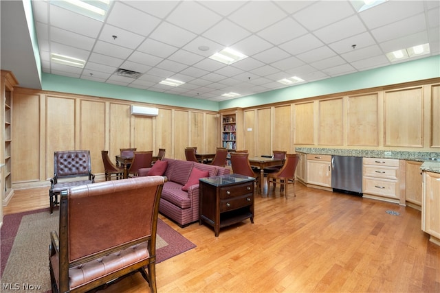 living room with a wall unit AC, light hardwood / wood-style flooring, and a paneled ceiling