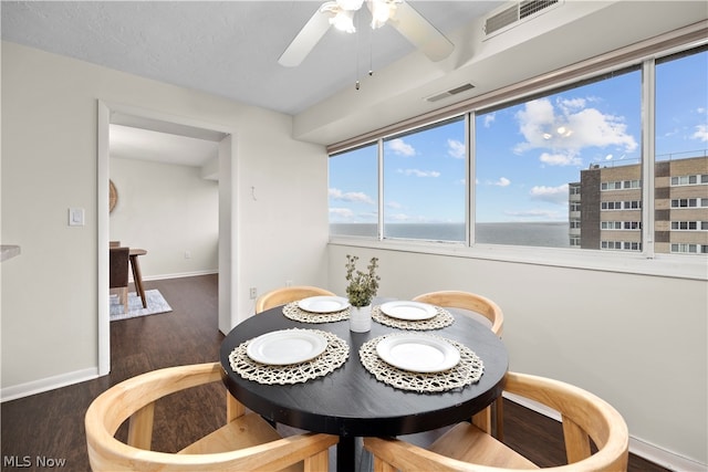 dining room with dark hardwood / wood-style floors, ceiling fan, and a water view