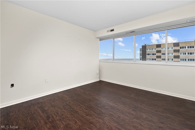 spare room featuring a healthy amount of sunlight and dark hardwood / wood-style flooring