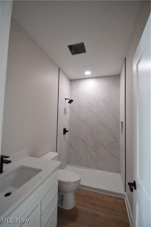 bathroom with vanity, wood-type flooring, toilet, and tiled shower