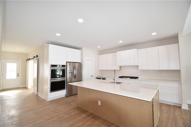 kitchen featuring appliances with stainless steel finishes, a barn door, a center island with sink, and white cabinets