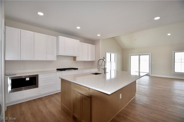 kitchen with sink, white cabinetry, stainless steel microwave, a center island with sink, and black gas stovetop