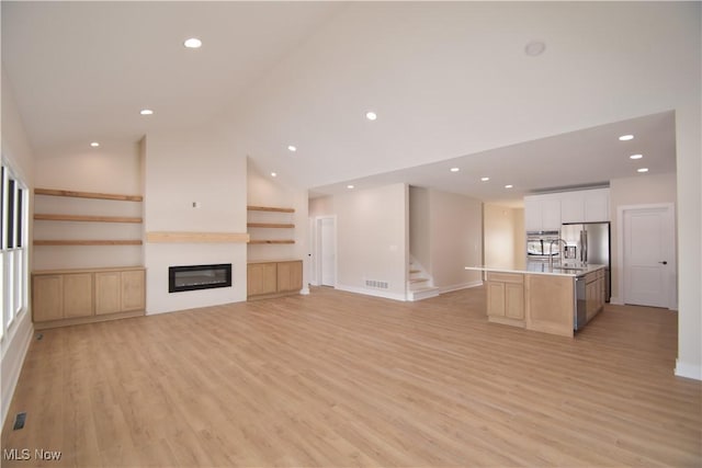 unfurnished living room featuring high vaulted ceiling, sink, and light hardwood / wood-style floors