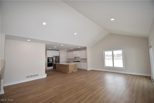 unfurnished living room with sink, hardwood / wood-style flooring, and high vaulted ceiling