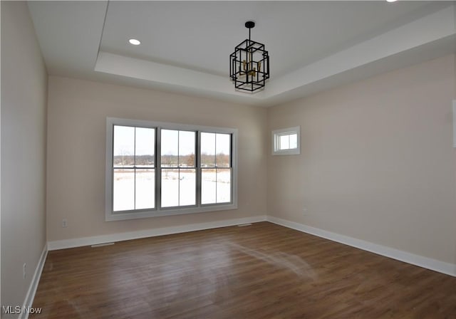 empty room with a raised ceiling, dark wood-type flooring, and a chandelier