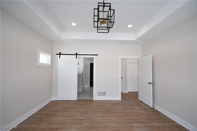 unfurnished bedroom featuring ensuite bathroom, a barn door, wood-type flooring, and a tray ceiling