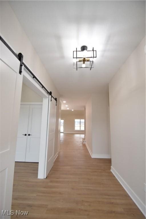 corridor with light wood finished floors, a barn door, and baseboards