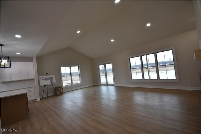 unfurnished living room featuring a chandelier, baseboards, wood finished floors, and lofted ceiling