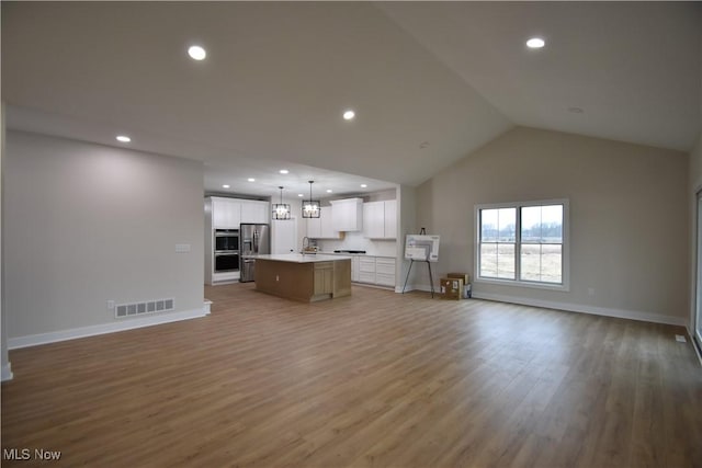 kitchen with visible vents, appliances with stainless steel finishes, open floor plan, an island with sink, and wood finished floors