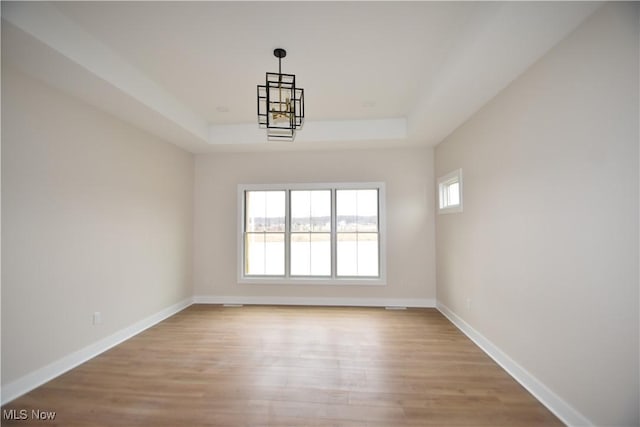 empty room with a chandelier, a raised ceiling, light wood-style flooring, and baseboards