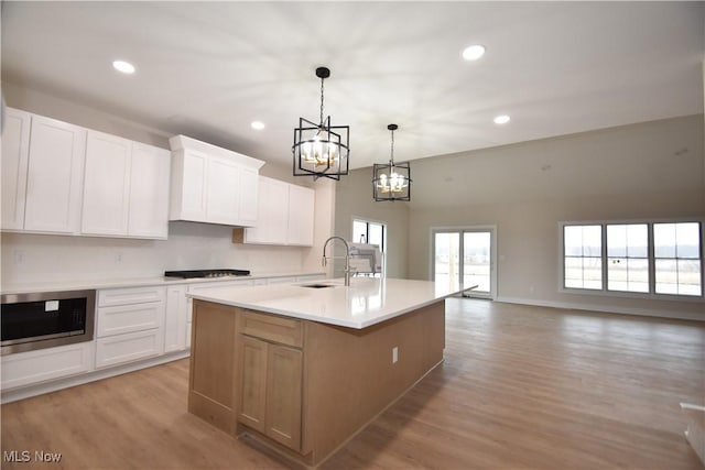 kitchen with a sink, white cabinetry, light countertops, light wood finished floors, and stainless steel microwave