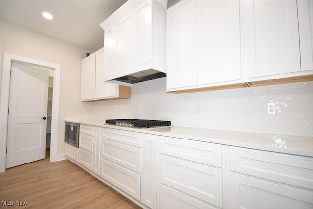 kitchen with light wood-style flooring, gas stovetop, white cabinetry, light countertops, and stainless steel microwave